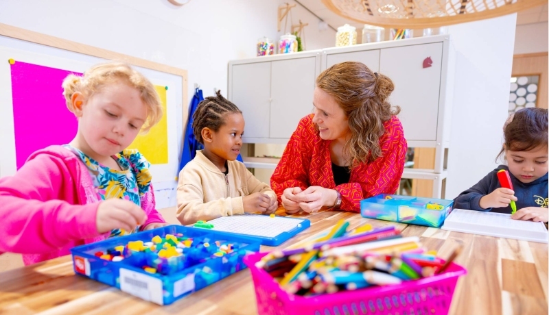 Omscholer naar basisonderwijs legt iets uit aan een kleuter in de klas.