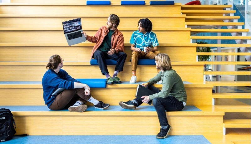 Docent CMD laat voorbeeld zien via zijn laptop aan studenten op de trap.
