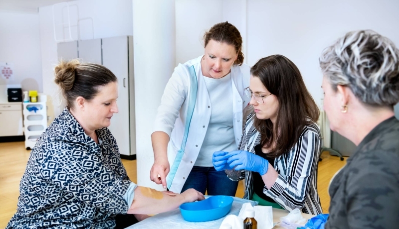 Docent geeft aan 3 studenten uitleg over wondverzorging tijdens les Verpleegkunde deeltijd