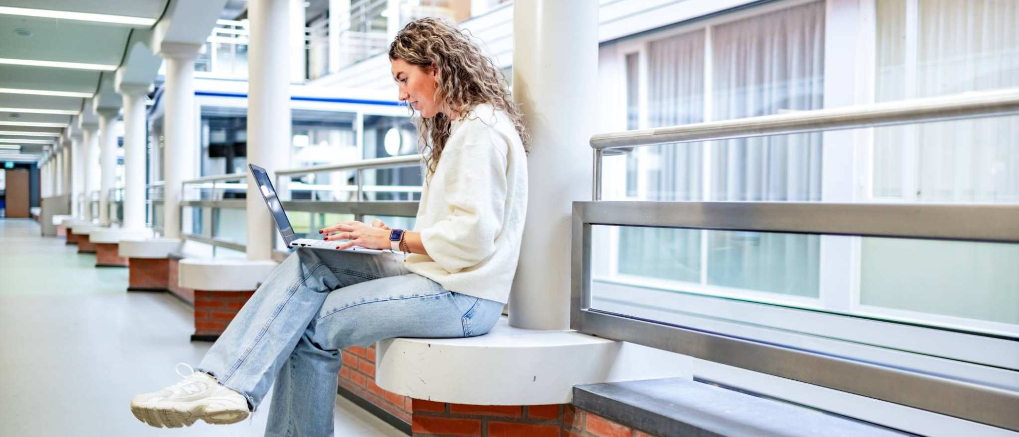 Student van de bachelor Commerciële Economie deeltijd, duaal in gang met laptop. 