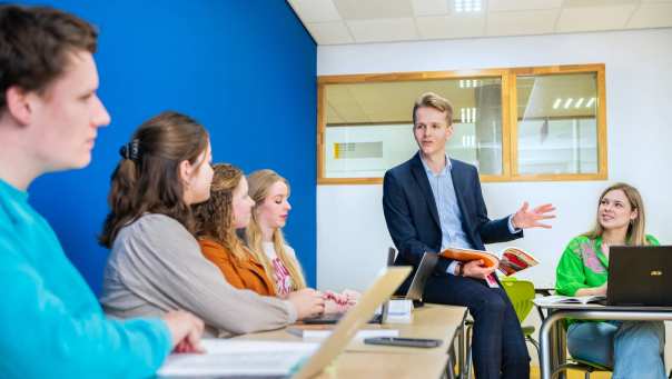 Duits docent bladert door studieboek en praat richting leerlingen