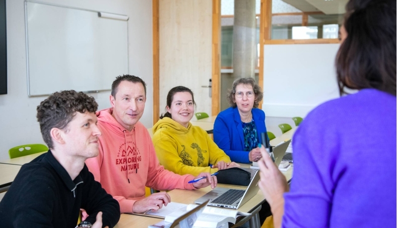 vier masterstudenten luisteren aandachtig naar een docent voor ze