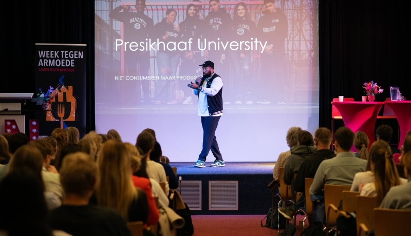 Volle zaal in Nijmegen met mensen in stoelen met voorraan een podium waarop Melvin Kolf, een jongen met een petje en baseball pet, zijn verhaal doet over Presikhaaf University