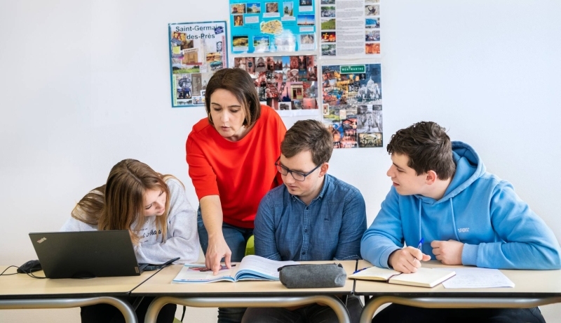 Twee studenten kijken lachend naar hun docent die tegenover hen zit.