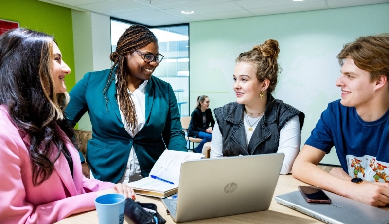 Studenten in overleg met een docent achter de laptop
