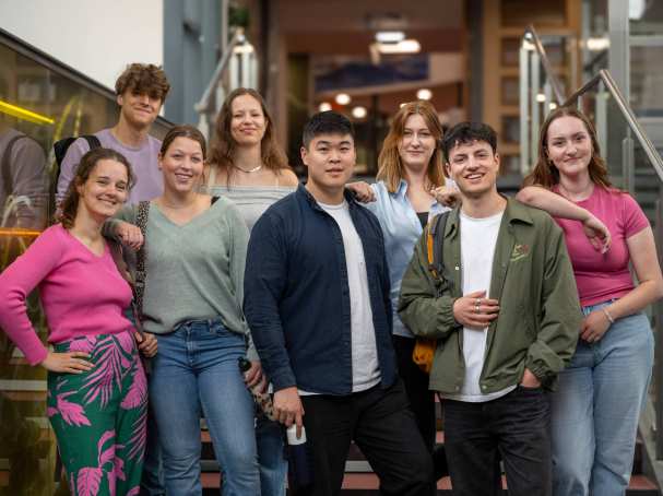 Groep studenten lachen in de camera, staan in de lichtstraat van gebouw R26.
