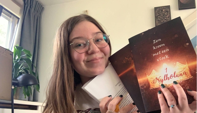 CMD-student Jade Vermeulen heeft haar eigen geschreven boeken in haar handen en glimlacht