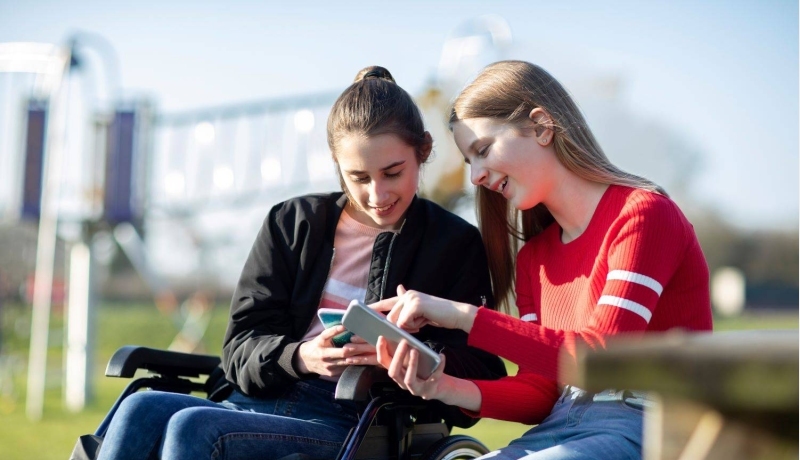 Tiener meisje in rolstoel kijkt naar mobiel met vriendin