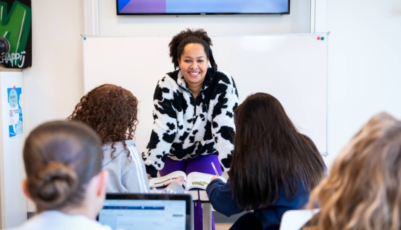 Docente Angel Olatunji leunt voorover op de lessenaar in een klaslokaal op het Citadel College.