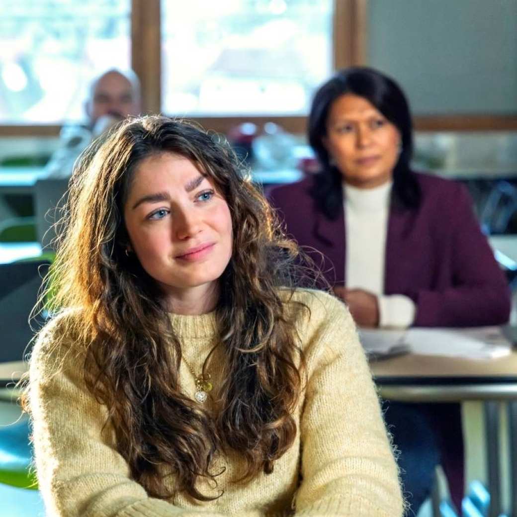 Cursisten zitten aan bureau's in een  leslokaal en luisteren aandachtig.