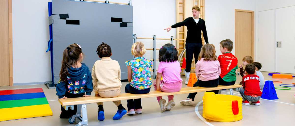 De kleuters op de school De Ommelander. De leraar wijst de kleuters iets aan in de gymzaal.