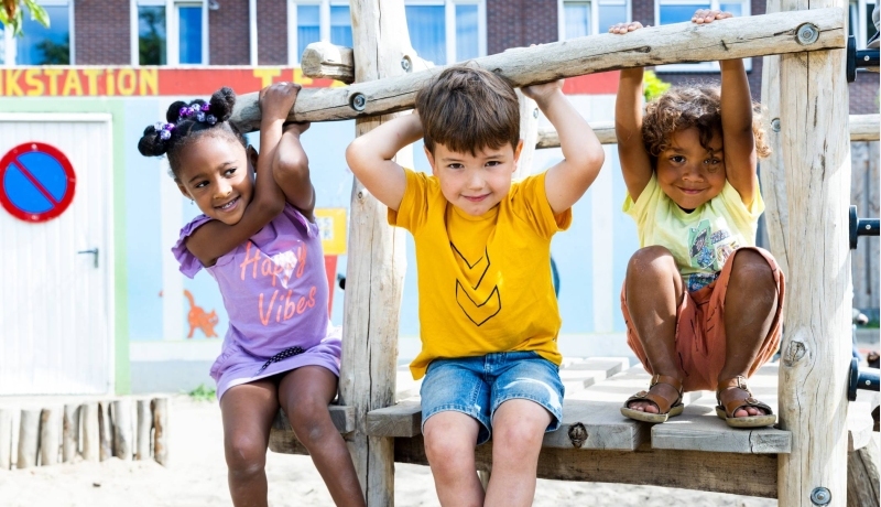 Drie kinderen spelen buiten en hangen aan het speelrek