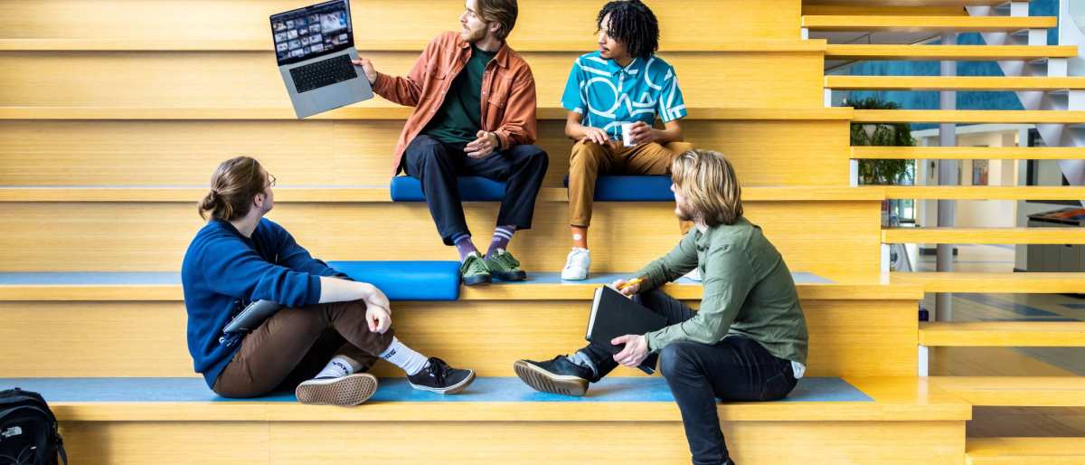 Docent CMD laat voorbeeld zien via zijn laptop aan studenten op de trap.