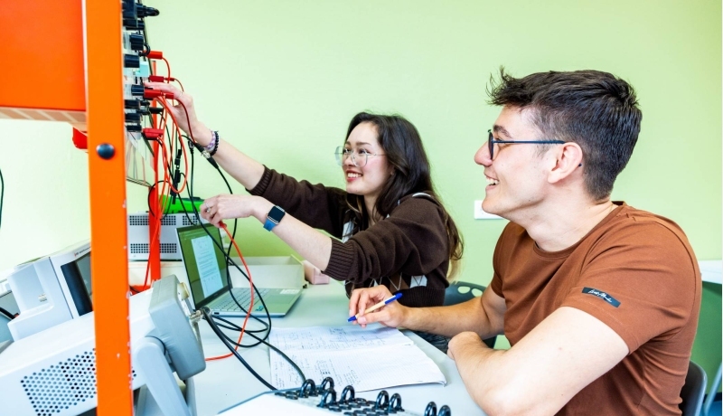 Twee studenten elektrotechniek werken samen aan een logboek tijdens een practicumsituatie.