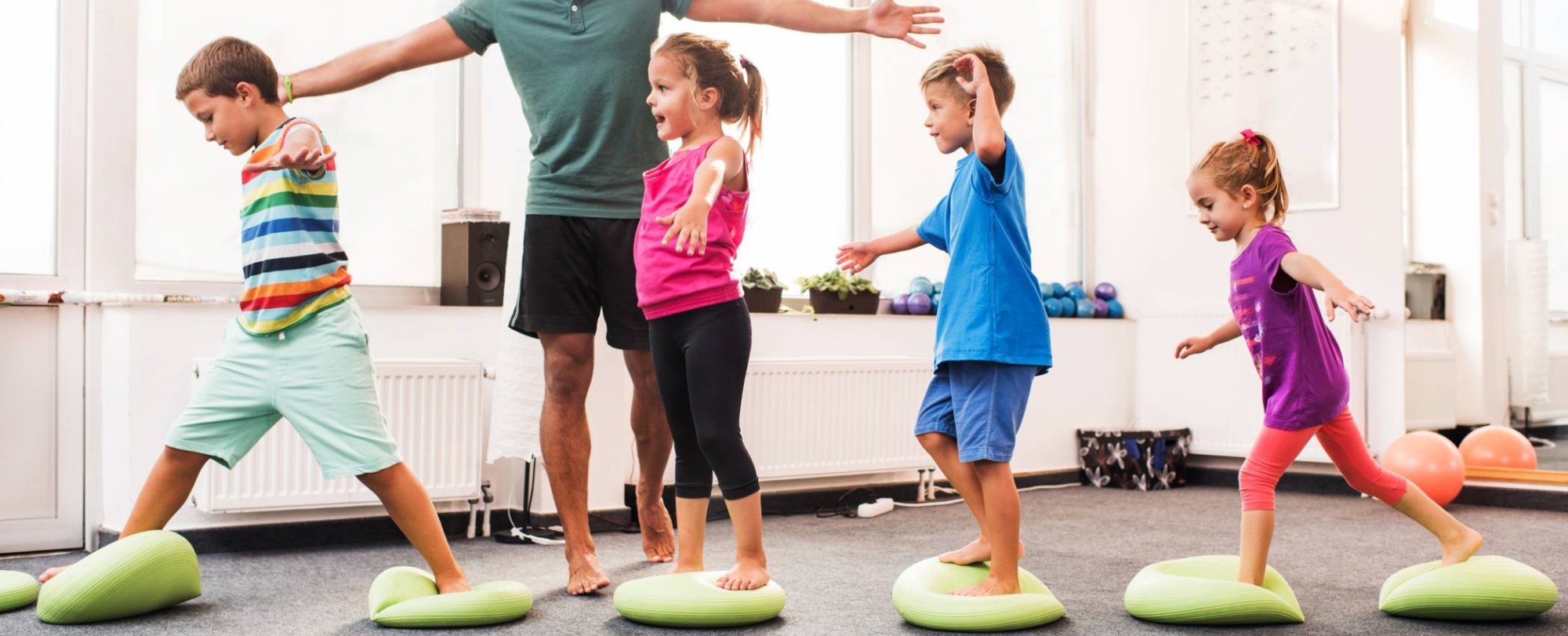 kinderen wandelen op pilates-ballen tijdens training op sportschool met mannelijke coach