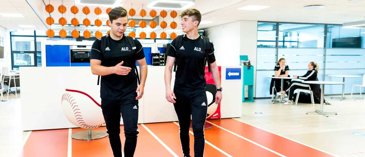 Twee jongens lopen in hun alo-tenue door de gang.