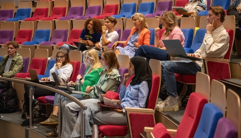 Grote groep studenten zitten in de collegezaal en luisteren naar hoorcollege. 