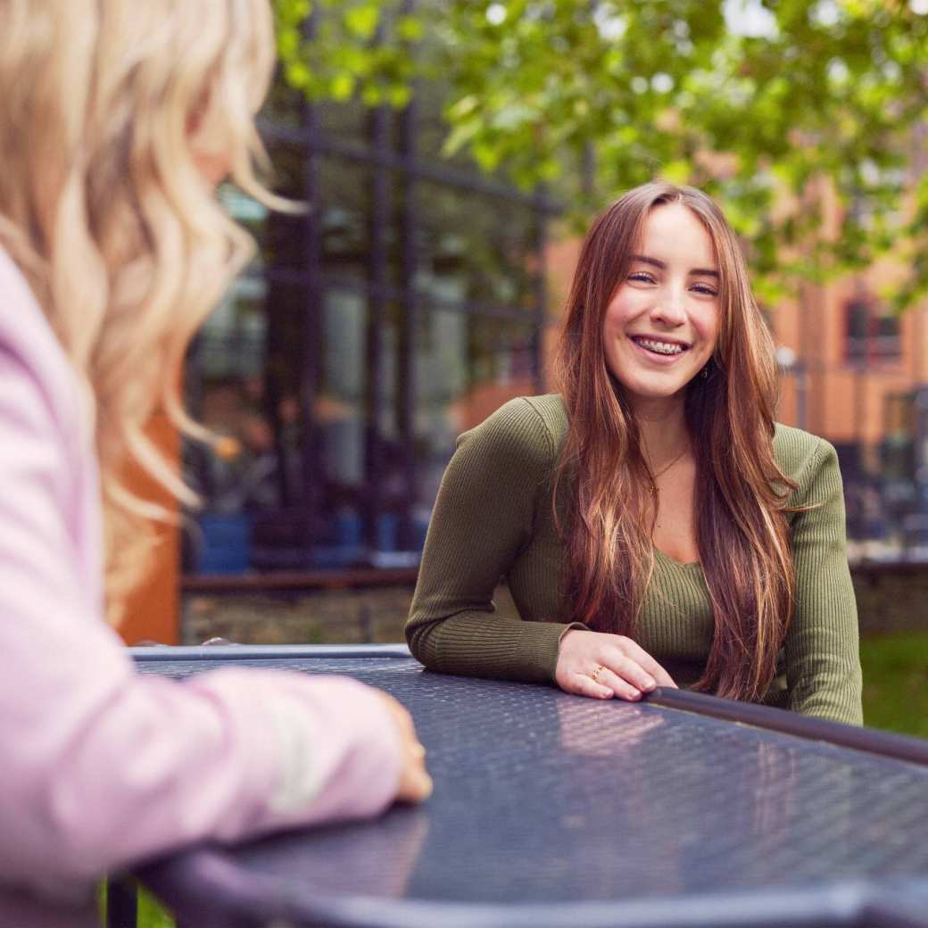 werving voltijd campagne, twee studentes in gesprek aan een picnictafel in de binnentuin.