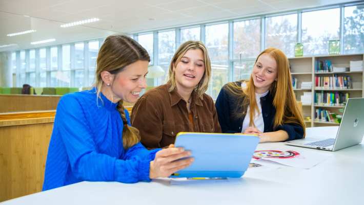 Drie mensen zitten aan een tafel met een tablet en een laptop en lachen.
