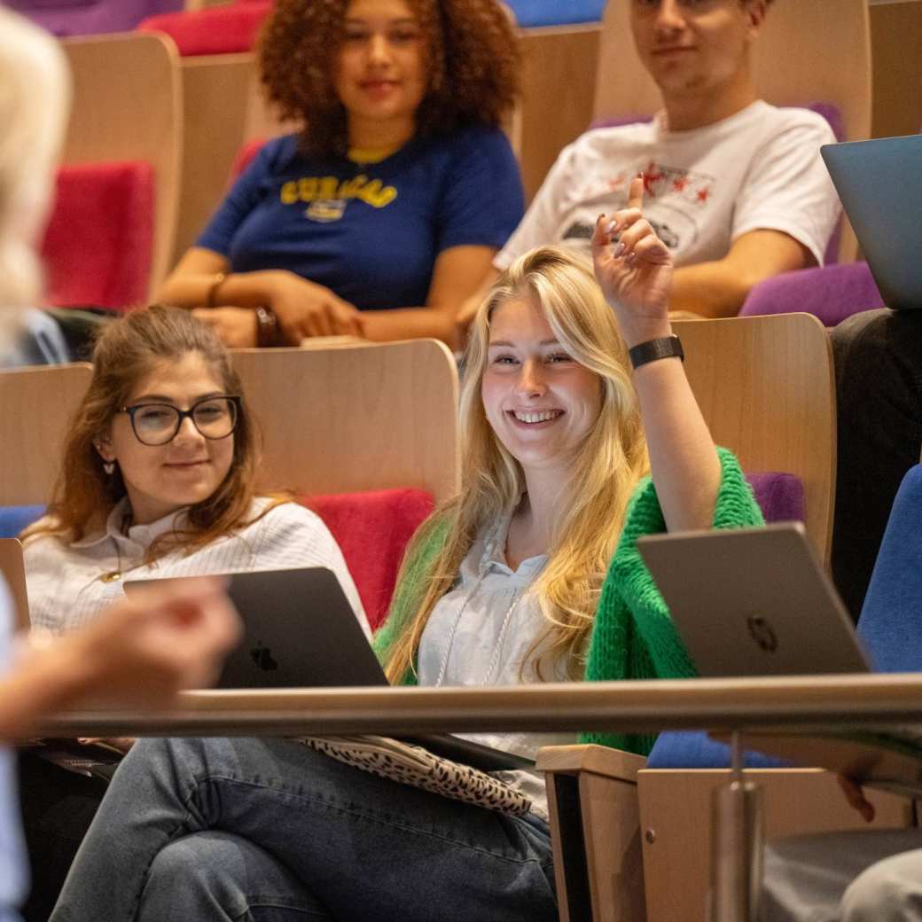 Studente steekt hand op tijdens hoorcollege in de collegezaal