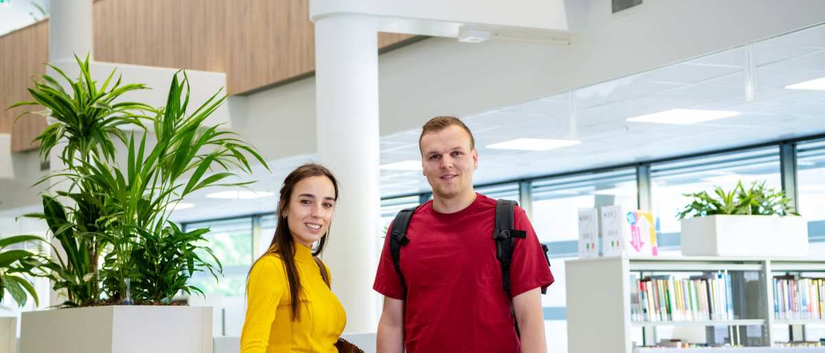 Twee studenten van de opleiding Bedrijfskunde deeltijd in gesprek in de bibliotheek in Arnhem, Ruitenberglaan 31. Ze lachen.