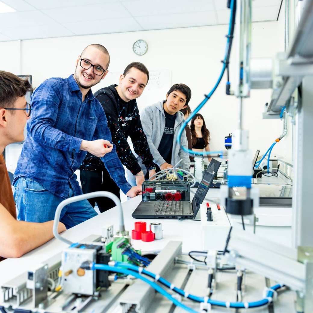 Docent en studenten elektrotechniek aan een Programmable Logic Controller (PLC).