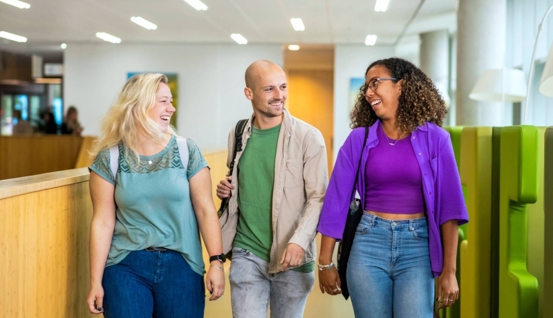 Drie studenten Leraar Wiskunde lopen lachend naast elkaar op de gang in de school