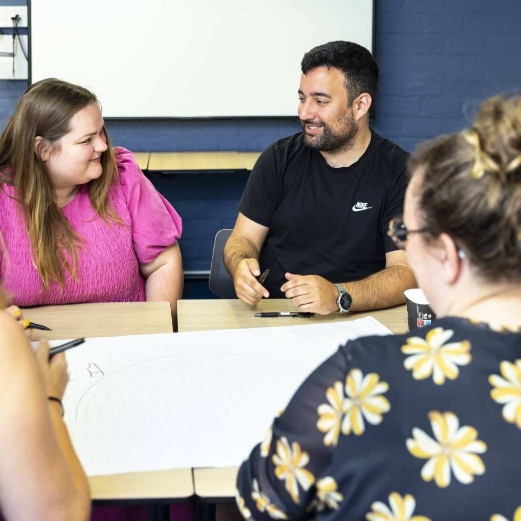Overleg master social work studenten. Vrouwelijke student met roze tshirt kijkt lachend naar man met zwart haar en zwart tshirt.