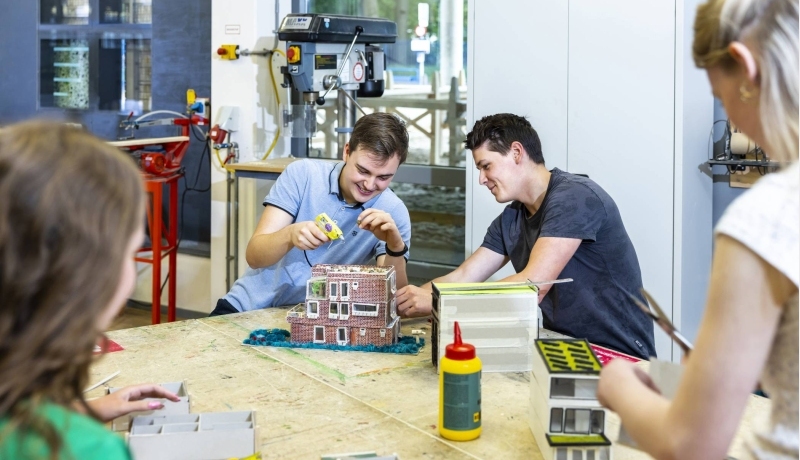 vier studenten zetten in de werkplaats van HAN Bouwkunde hun houten maquettes met houtlijm in elkaar