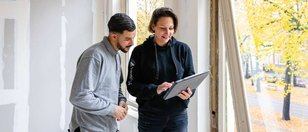 bouwkundige bespreekt bij een venster de voortgang met een medewerker