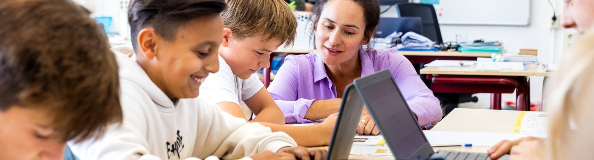 De lerares van de opleiding leraar basisonderwijs legt iets persoonlijk uit aan een leerling aan zijn tafel.