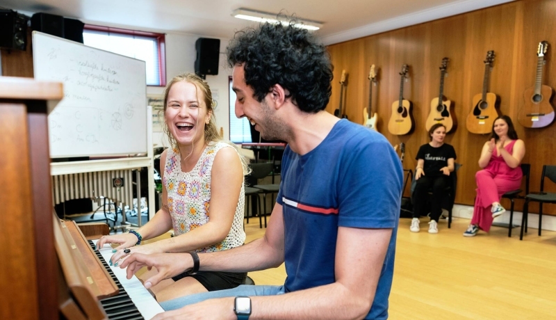Twee studenten muziektherapie spelen samen op de piano tijdens een praktijkles
