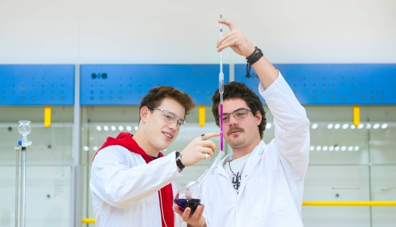 Twee studenten Leraar Scheikunde voeren een experiment uit en hebben een labjas aan en een veiligheidsbril op.