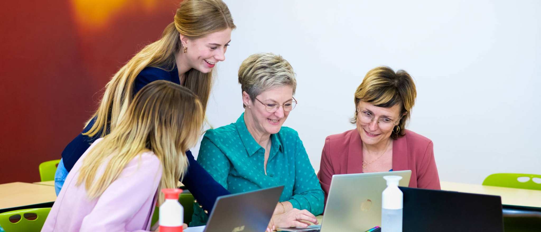 Vier studenten kijken samen op één scherm, terwijl iedereen een laptop heeft.
