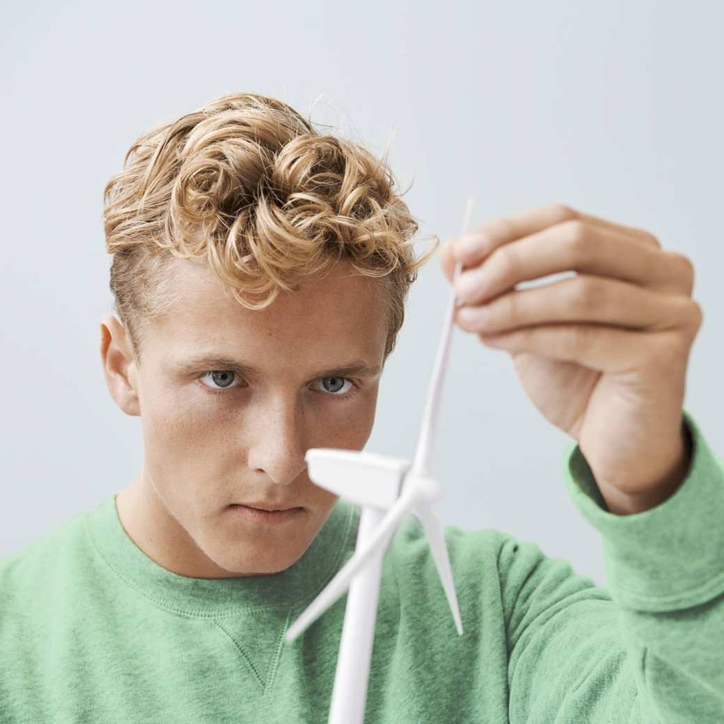 jongen met groene trui en blonde haren die bij een model windmolen zit