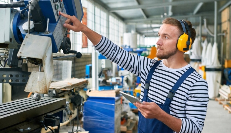 Jonge operator met gele gehoorbeschermers op de werkvloer van een moderne fabriek