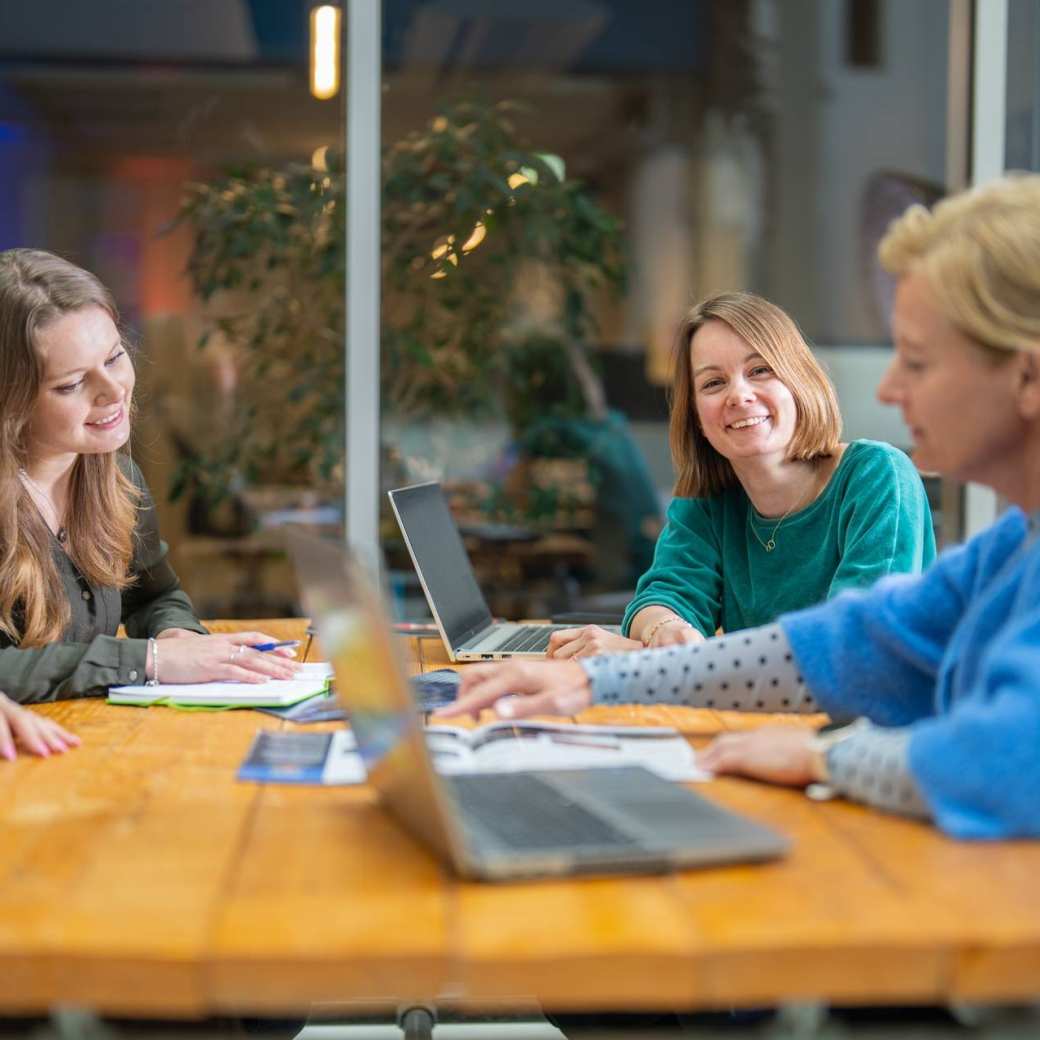 3 studenten en één docent van de master Duurzaamheidstransities zitten aan een tafel en overleggen. Eén student kijkt in de camera en lacht.