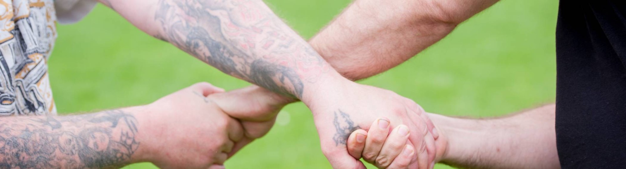 Twee personen die handen vasthouden kruislings voor het lichaam. Je ziet geen hoofden.