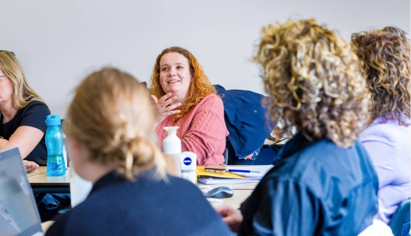 Vrouw in roze trui is in gesprek met docent tijdens de cursus acute pijn service.