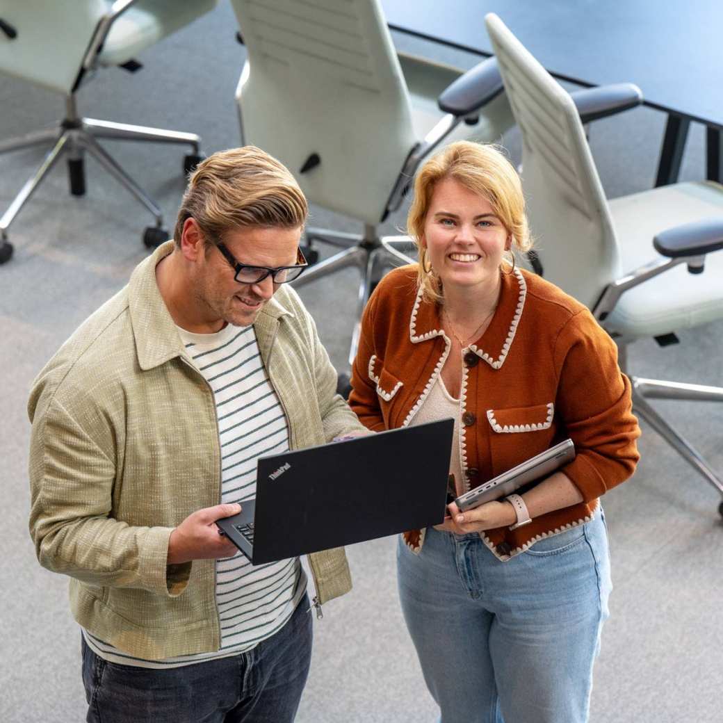 Man en vrouw staan met laptop in de hand en kijken lachend naar camera