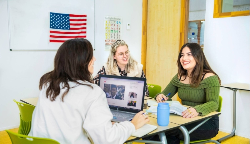 Docent geeft les aan haar drie studenten in een lokaal met de Engelse vlag aan de muur.