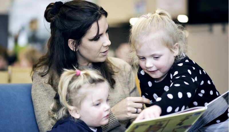 Vrouw laat aan twee kinderen een boek zien.