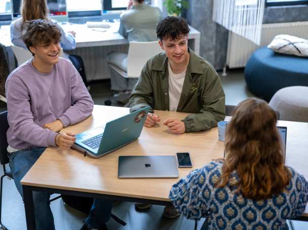 Studenten zitten in een klas en werken samen aan tafel, ze hebben plezier.