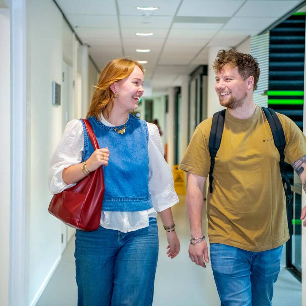 Jongen en meisje lopen in de gang op de HAN campus in Nijmegen en kijken lachend naar elkaar.