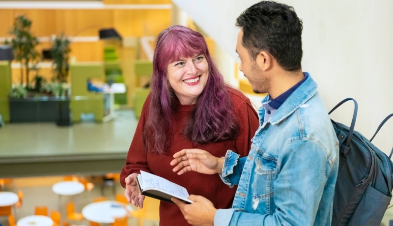 Twee studenten vertellen met elkaar terwijl de een een kladje in de hand heeft met geschreven tekst.