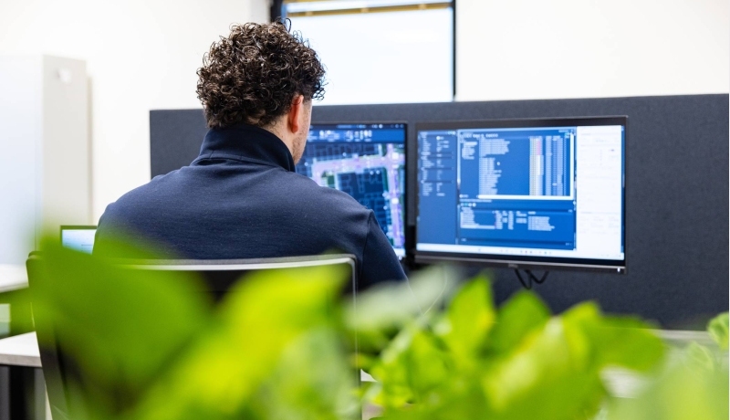 Man werkt op twee beeldschermen aan een bouwontwerp. Op de voorgrond staat een plant