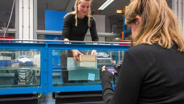 Nienke Maas en Brechtje Kraaijvanger doen een proef in het waterlab met het model van een woonboot