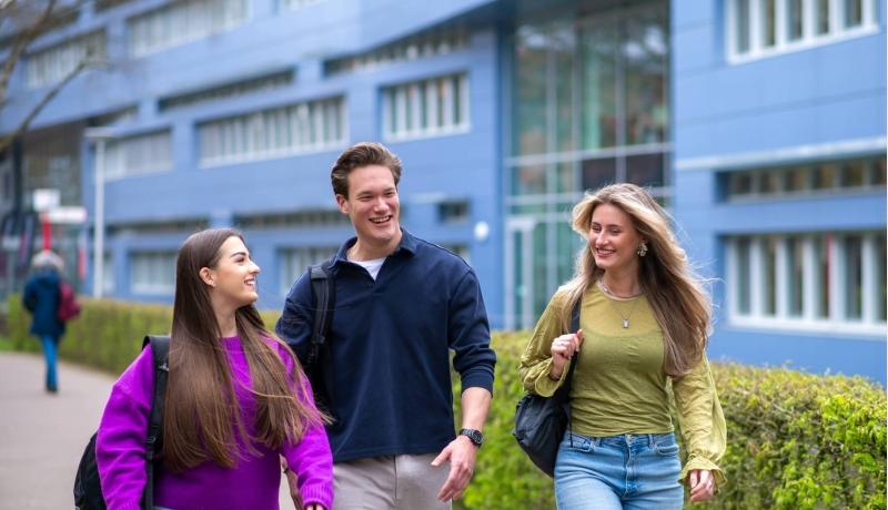 Drie studenten van Learning and Development in Organisations voltijd lopen lachend voor het HAN gebouw in Nijmegen.