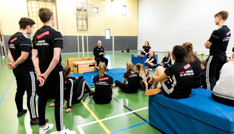 Pabo-ALO studenten zitten in de gymzaal rondom de docent die instructies geeft.