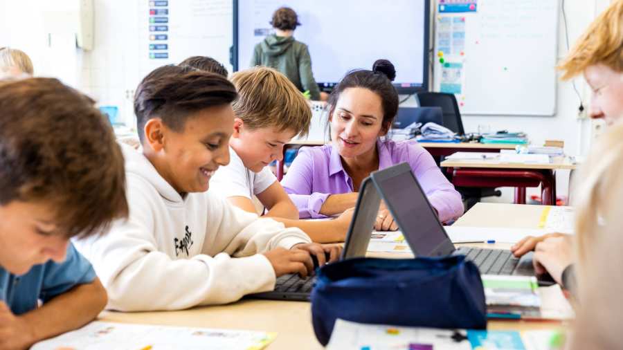 De lerares van de opleiding leraar basisonderwijs legt iets persoonlijk uit aan een leerling aan zijn tafel.
